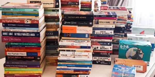 A pile of books on a table in front of a window.