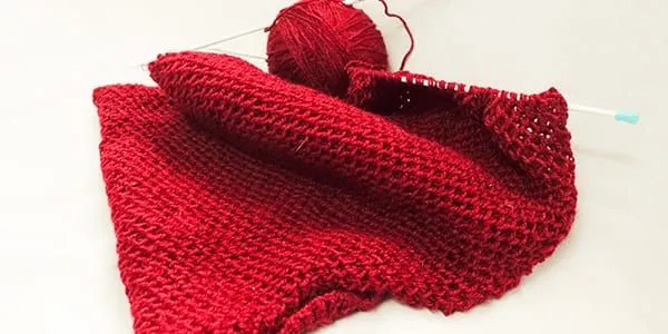 A red knitted blanket on a white surface.