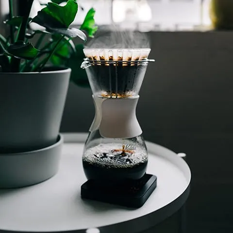 A coffee maker sitting on a table next to a plant.