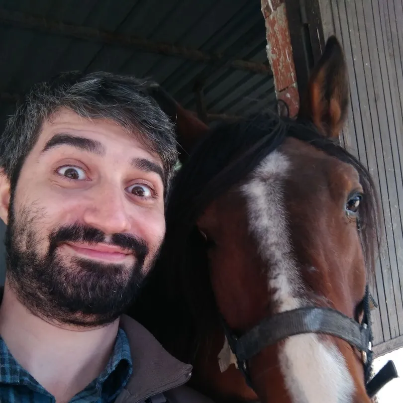 A man with a beard is standing next to a horse.