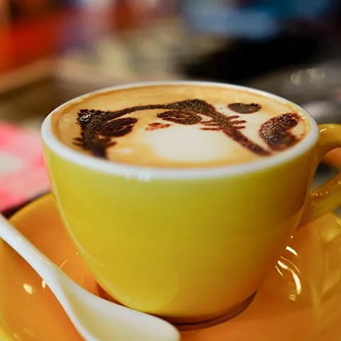 A cup of coffee with a cat drawn on it.