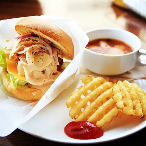 A burger and fries on a plate next to a cup of soup.