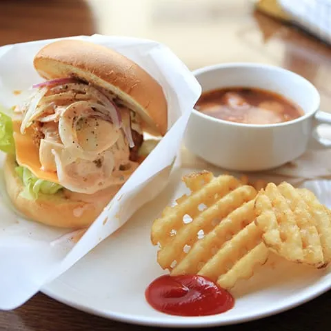 A chicken burger with fries and a cup of soup.