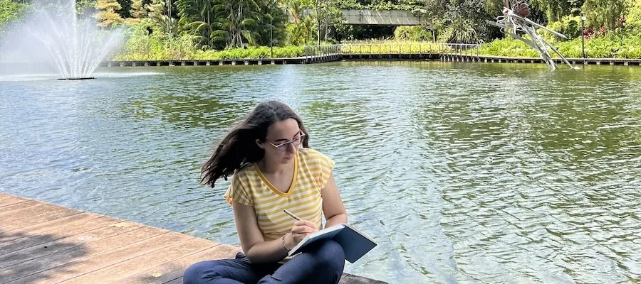 A woman sits on a wooden bench next to a pond.